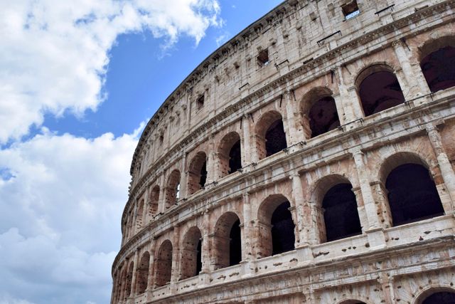 Depicts the iconic outer arches of the Colosseum against a partly cloudy sky. Ideal for travel blogs, educational materials on ancient Roman history, architectural magazines, and tourism advertisements related to Italy.