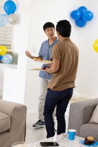 Two asian men carrying appetizer platters and chatting at casual home party