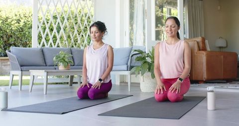 Two women meditating on sunlit patio in matching pink tops and yoga leggings for wellness