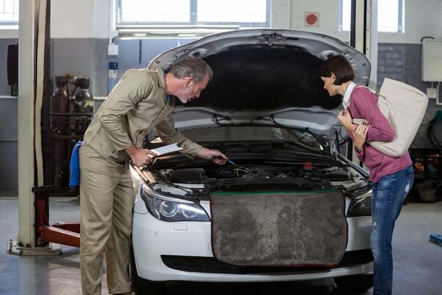 Mechanic showing car issues to customer in auto repair shop. Ideal for content related to automotive services, customer service in auto repair, vehicle maintenance, and professional car inspections.