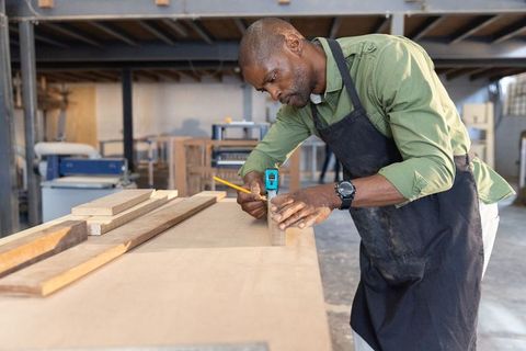 African american carpenter measuring wood with tape and pencil in workshop precision joinery