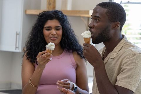 Diverse couple sharing vanilla waffle cones in sunlit kitchen, tasting summer dessert