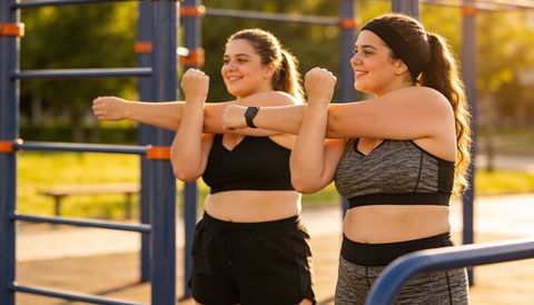 Plus-size women stretching arms at outdoor calisthenics park during golden hour workout