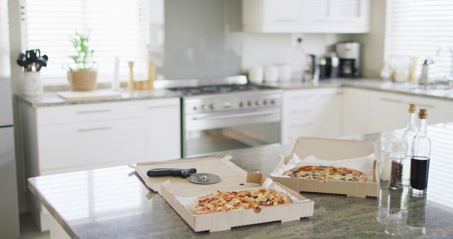 Two fresh pizzas sit on the countertop of a modern home kitchen. A pizza cutter and bottles of condiments are also present. This scene is perfect for depicting home dining, family meals, food delivery, or culinary themes.