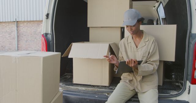 Young biracial woman checks inventory on a tablet beside a delivery van. She's ensuring accuracy for the shipment at an outdoor loading area.