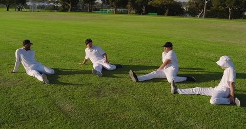 Cricket Players Stretching on Sunlit Outfield Warming Up Together Before Match