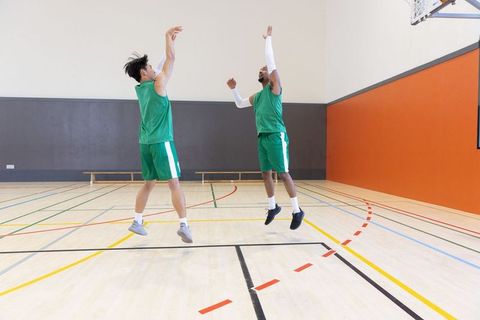 Asian and african american basketball teammates jumping and contesting shot on indoor court