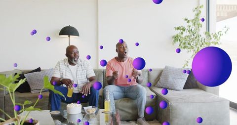 Multigenerational black family watching game and reacting amid floating purple spheres