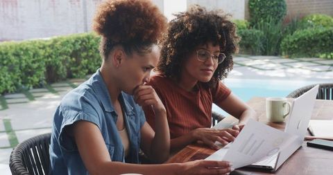 Two African American Women Reviewing Financial Charts on Laptop Poolside, Collaborating