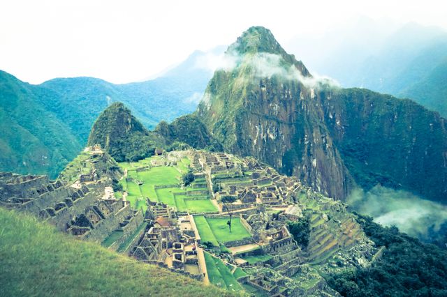 This image showcases a stunning aerial view of the iconic Inca ruins of Machu Picchu amidst the Andes Mountains in Peru. The lush green terraces and dramatic mountain backdrop highlight the historical significance and natural beauty of this UNESCO World Heritage site. Perfect for use in travel blogs, tourism agencies, educational materials, and adventure promotions.