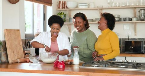 Three women enjoying cooking together in warm kitchen setting