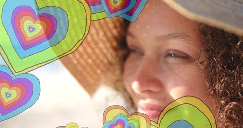 Joyful mixed heritage woman on sand beach with colorful hearts