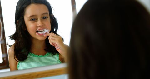 Young girl brushing teeth in bathroom mirror reflection