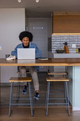 African american man working remotely at kitchen island with laptop and headphones