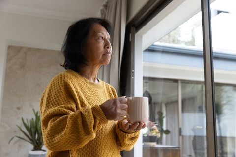 Senior Woman Holding Mug and Gazing Out Window in Tranquil Setting