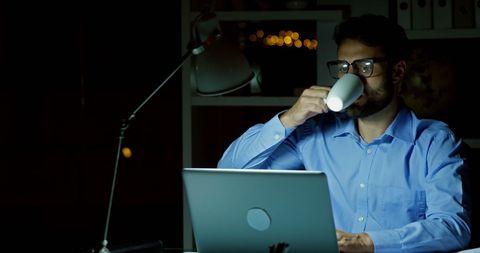 Young Caucasian Man Working Late Night at Laptop with Coffee