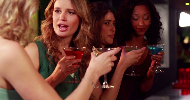 A diverse group of young women enjoy colorful cocktails at a bar, with copy space. Their expressions and body language suggest a lively conversation and a fun night out.
