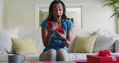 Surprised Woman Opening Gift Box on Sofa at Home