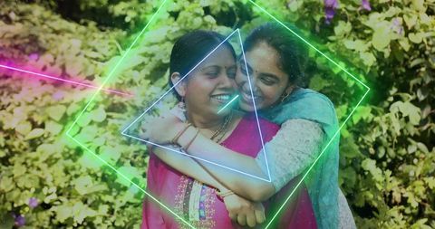 Indian mother and adult daughter hugging in garden wearing kurta and dupatta with neon overlays