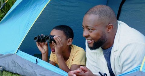 African american father and son camping bonding peering through binoculars from tent
