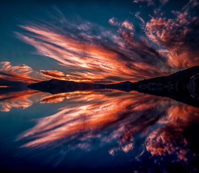 Picture showcases a breathtaking vibrant sunset reflecting on a calm lake surrounded by hills. The vivid colors of the sky and mirrored water create a serene and picturesque scene. Ideal for use in travel blogs, nature-themed websites, relaxation retreats, desktop wallpapers, and calendars emphasizing natural beauty and tranquility.