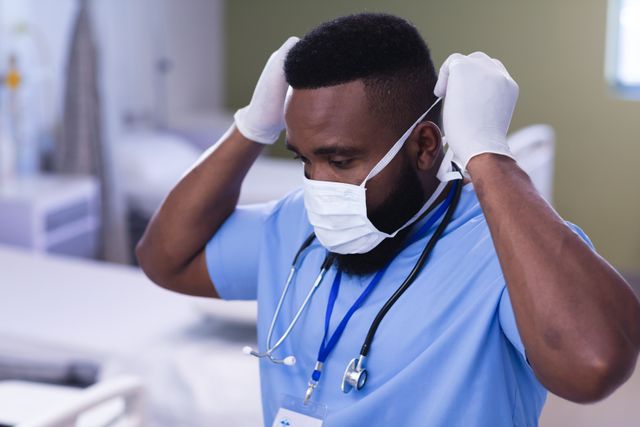 African american male doctor putting on face mask in hospital ward. Medical services, hospital and healthcare concept.