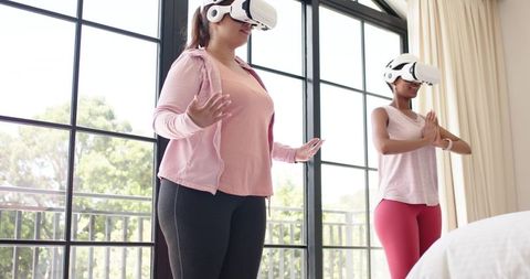 Women Meditating with VR Headsets in Bright Bedroom Practicing Virtual Yoga