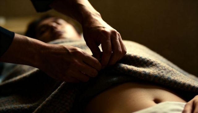 Hands fastening soft wool blanket over resting person abdomen intimate tenderness closeup