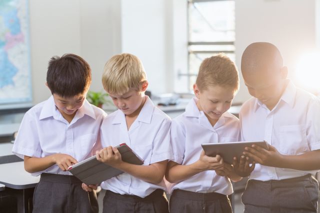 Diverse group of young boys in school uniforms using digital tablets in a bright classroom. Ideal for educational content, technology in education, modern learning environments, and teamwork concepts.