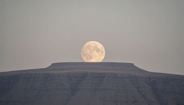 Full moon rising over flat-topped mesa at twilight, minimalist lunar plateau landscape