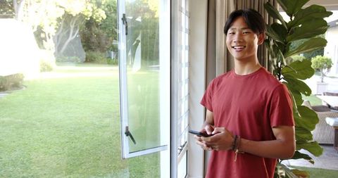 Smiling teen boy using smartphone by open sliding door at home