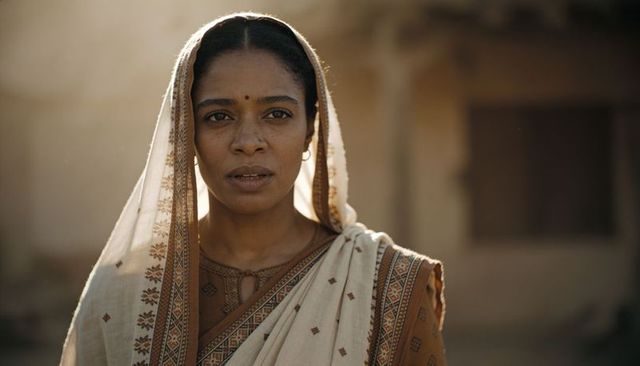 Sunlit indian woman standing in beige saree with pallu over head, contemplative portrait