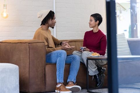 African american couple chatting on brown leather sofa sharing coffee in cozy lounge