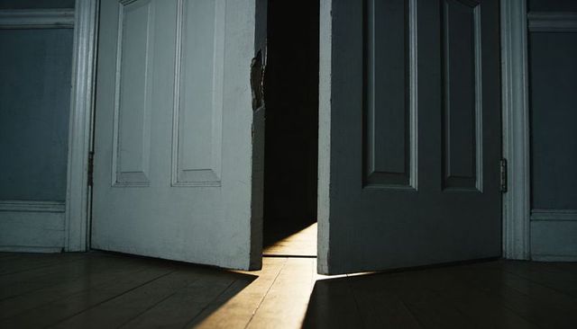 Warm sunbeam slicing through ajar white paneled double doors casting moody shadow