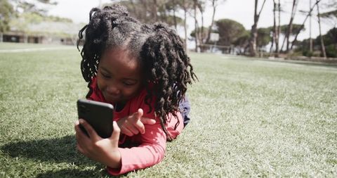 Joyful african american child enjoying smartphone in sunny park