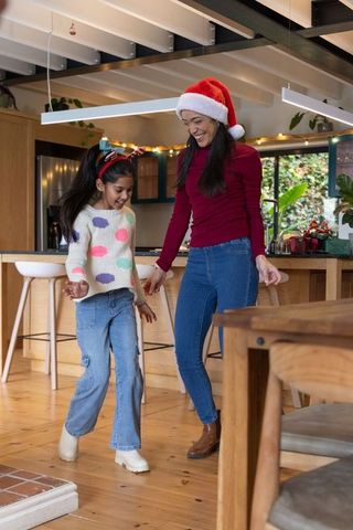 Mother and daughter dancing in cozy kitchen wearing santa hat and reindeer antlers