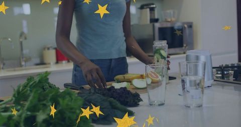 Preparing green smoothie at kitchen island with kale, fruits and gold star overlay