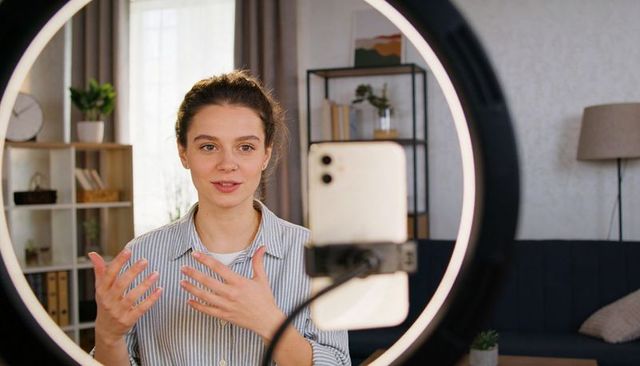 Young female creator talking to camera in cozy home studio with ring light and smartphone
