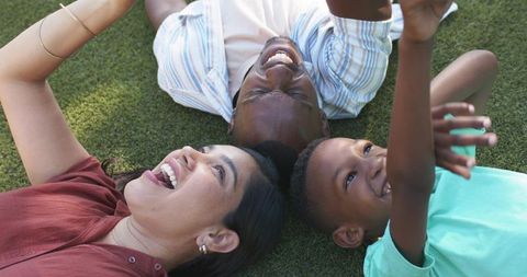 Joyful family lying on grass, smiling and looking up together in sunlit park
