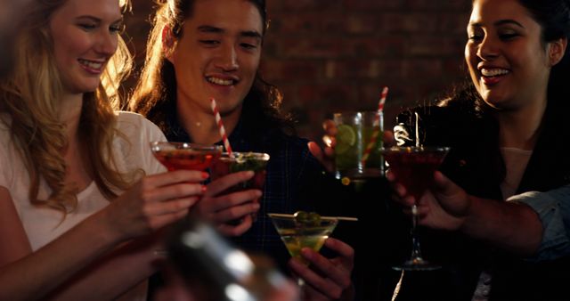 Young adults toasting with cocktails, enjoying night out together. Ideal for ads and articles about nightlife, social gatherings, bars, and celebrating occasions. Conveys festive and cheerful atmosphere.