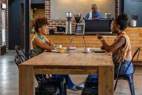 African american women collaborating at cafe table with laptops and coffee
