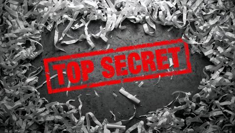 Red top secret stamp surrounded by shredded paper strips on dark grunge surface