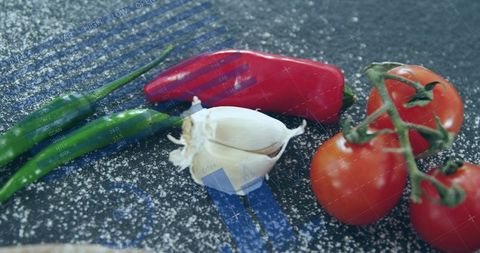 Tomato Cluster with Peeled Garlic, Red and Green Chilies on Dark Slate with Flour and Blue Overlay