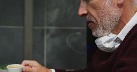 Man Relaxing Outside Cafe, Enjoying Coffee with Face Mask Pulled Down