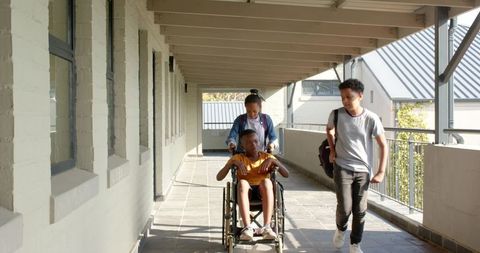 Students supporting classmate in wheelchair traveling school corridor