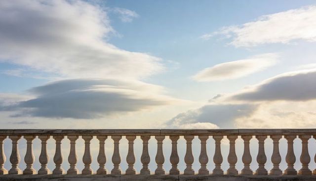 Sunlit Classical Stone Balustrade Framing Pale Blue Sky and Lenticular Clouds Over Terrace