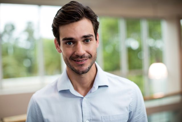 Young male business executive smiling confidently at a conference center. Ideal for use in corporate websites, business presentations, career development materials, and professional networking profiles.