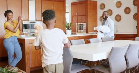 African american family clapping in modern kitchen while child holds teddy bear