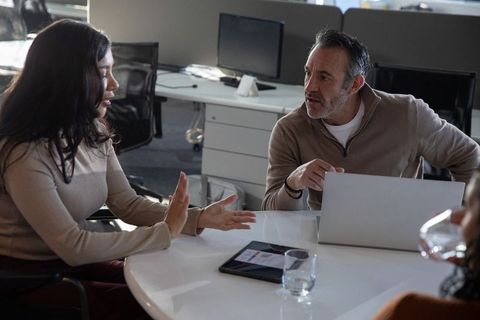 Diverse team collaborating around round table with laptop and tablet in modern office