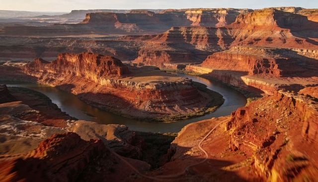 Golden hour revealing winding river meander around flat-topped sandstone butte in canyon